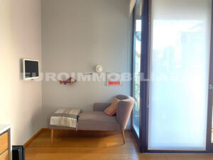 Angolo relax in un pentalocale a Milano con divano moderno, lampada da parete e una grande finestra.