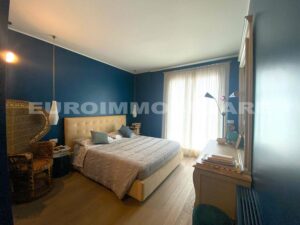 Camera da letto elegante con pareti blu e ampia finestra in un quadrilocale a Milano.